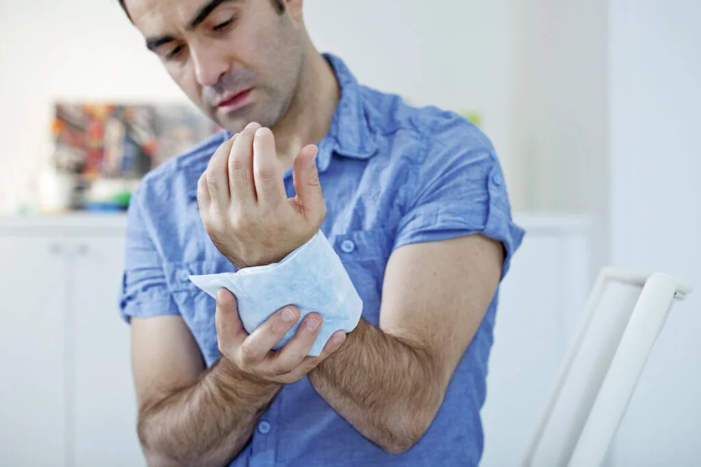 Man in blue shirt examining hand injury or wound wrapped in bandage