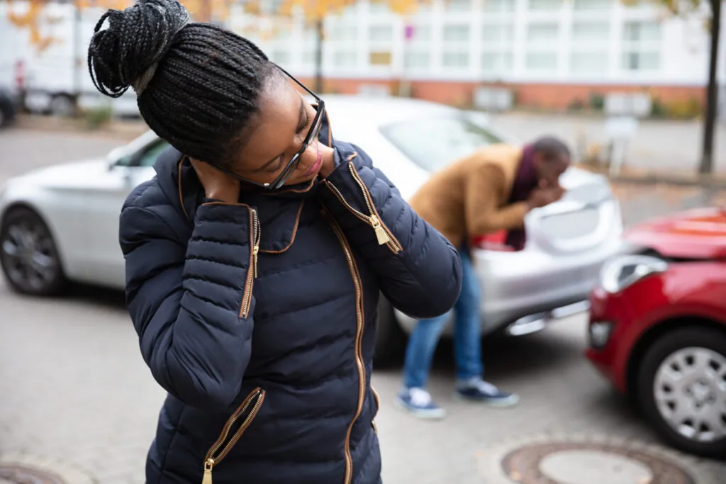 Person in navy puffer jacket and glasses stands in parking lot near parked cars