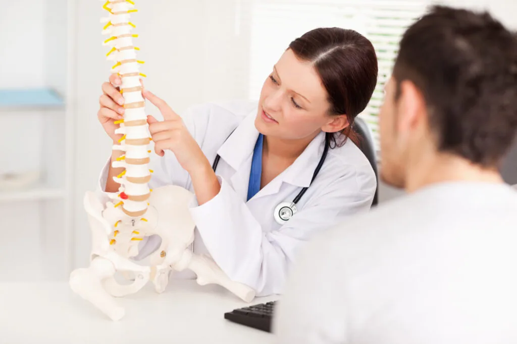 Doctor in white coat with stethoscope explaining spinal anatomy model to patient