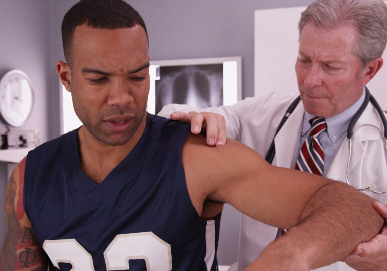 Middle aged male physician treating young male adult athlete's injury.
